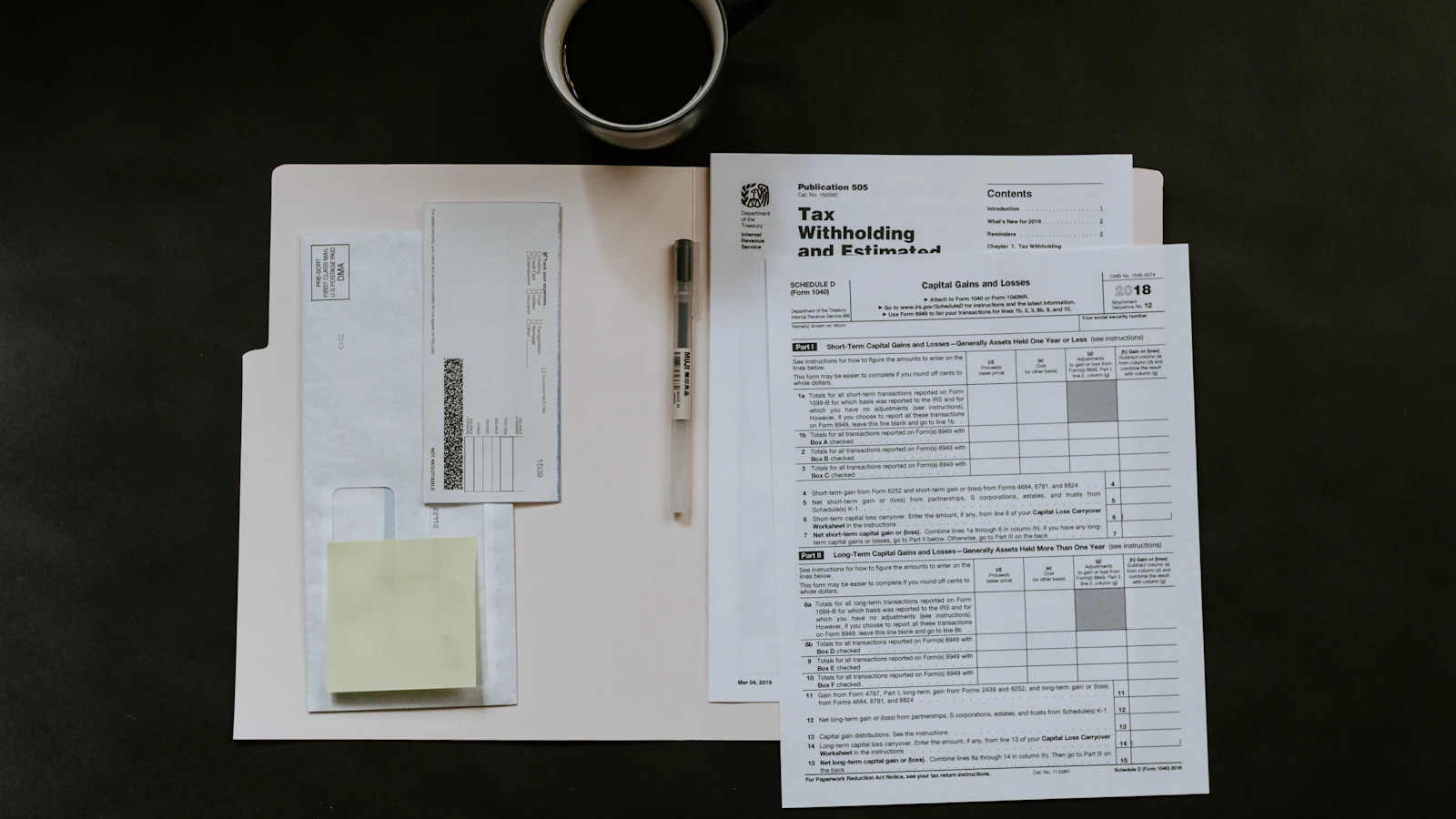 Tax forms, a pen, and a coffee mug arranged on a dark wooden desk