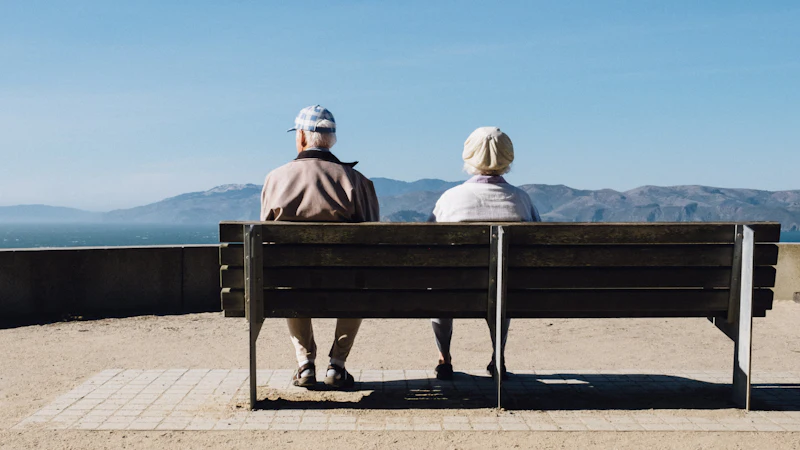 An older couple sitting on a bench looking out at the sea