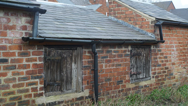An old brick outbuilding with boarded-up windows and a slate roof, evoking a vacant, unoccupied property