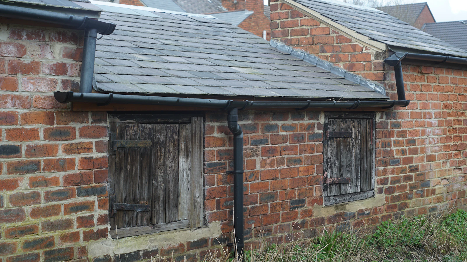 An old brick outbuilding with boarded-up windows and a slate roof, evoking a vacant, unoccupied property