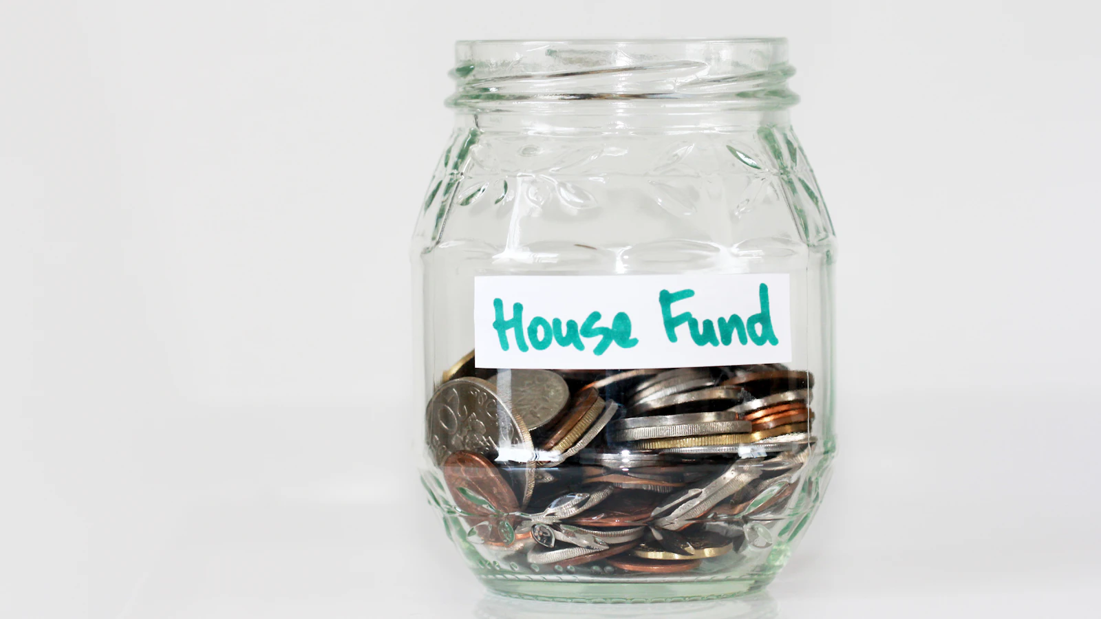 Coins in a clear glass jar with a house fund sign